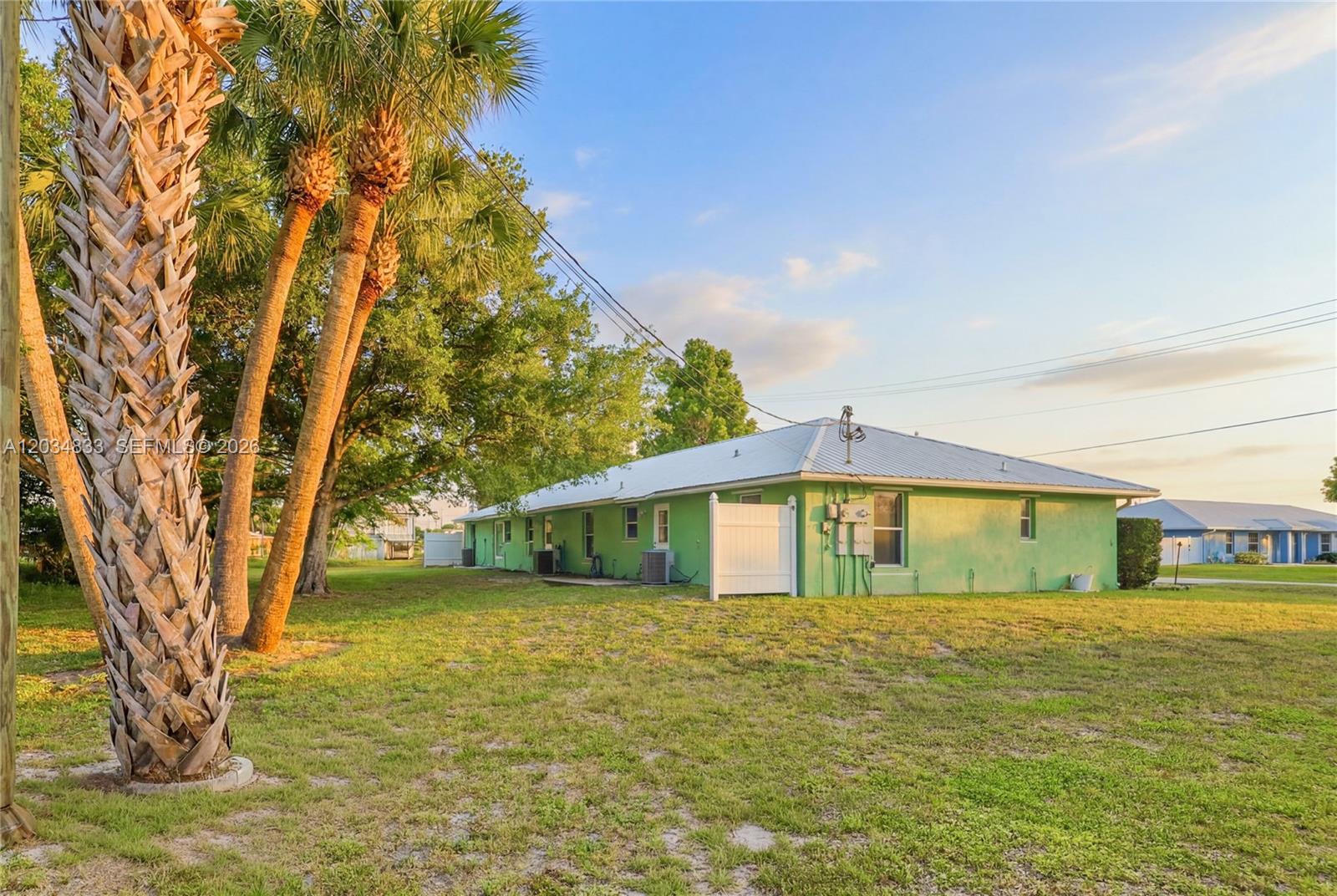 The exterior of a lime green, single-story house with a metal roof and palm trees — 810 SW 2nd St, Okeechobee FL 34974, OKEECHOBEE, FL