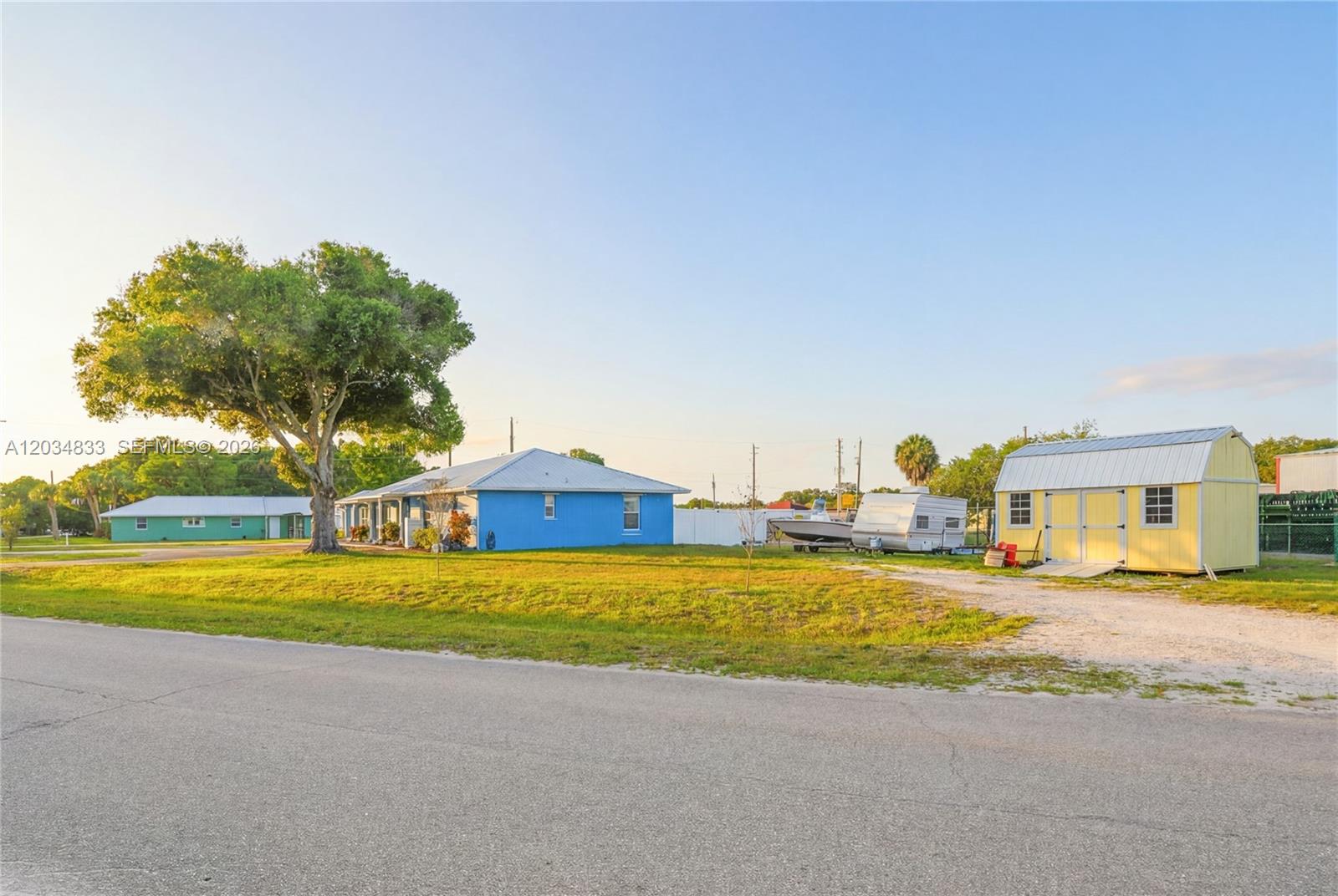 A blue house and a yellow shed sit on a grassy lot with a tree — 810 SW 2nd St, Okeechobee FL 34974, OKEECHOBEE, FL