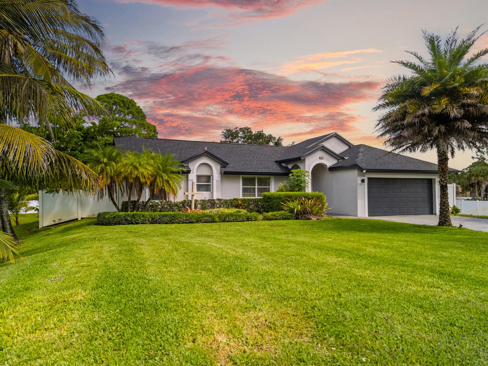 A single-story house with a dark roof, gray exterior, and palm trees at sunset — 16857 90th Street N, FL 33470, FL