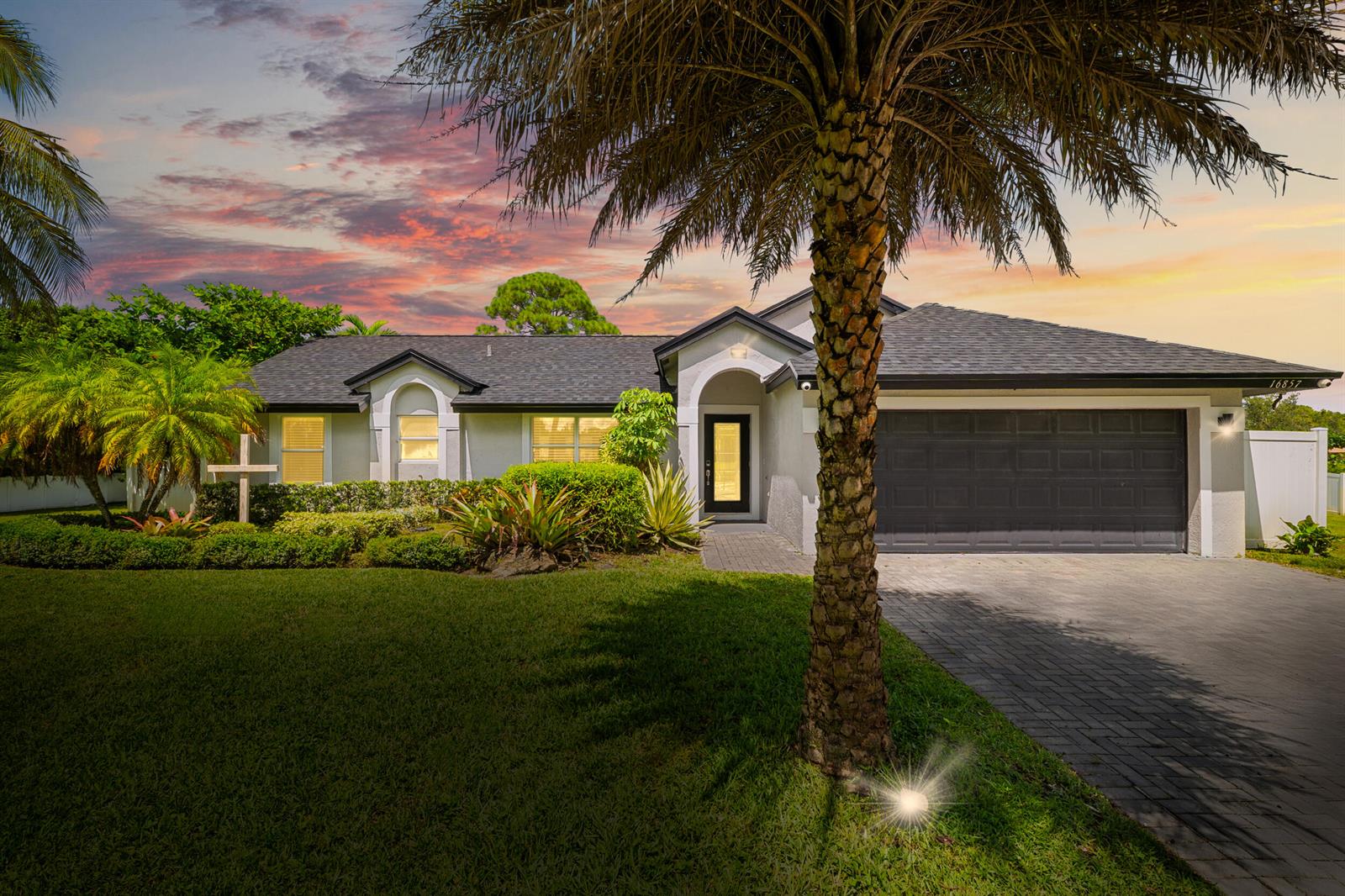 A single-story house with a gray roof, dark garage door, and a prominent palm tree — 16857 90th Street N, FL 33470, FL