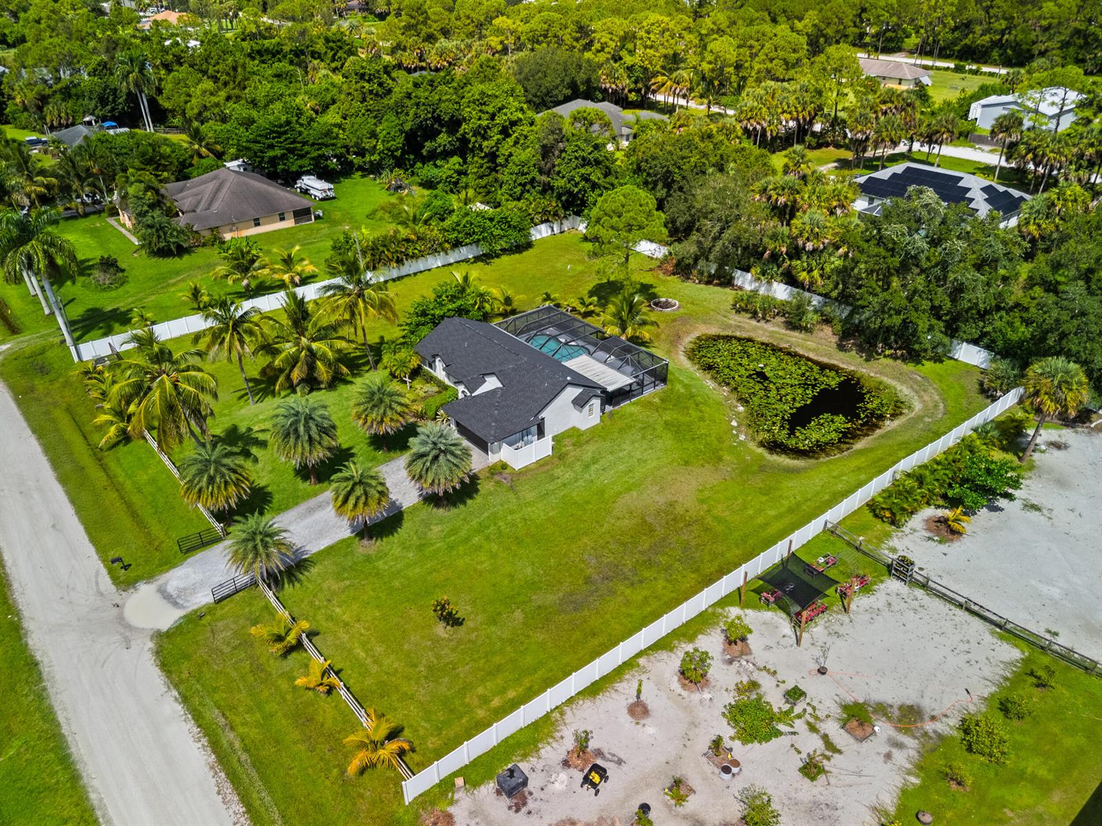 An aerial view shows a house with a pool enclosure, a pond, and palm trees — 16857 90th Street N, FL 33470, FL