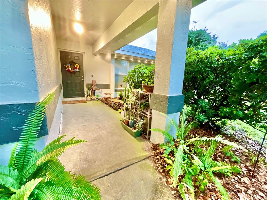 A covered front porch features a dark green door, potted plants, and a concrete walkway — 20517 NE 114TH AVENUE, WALDO, FL