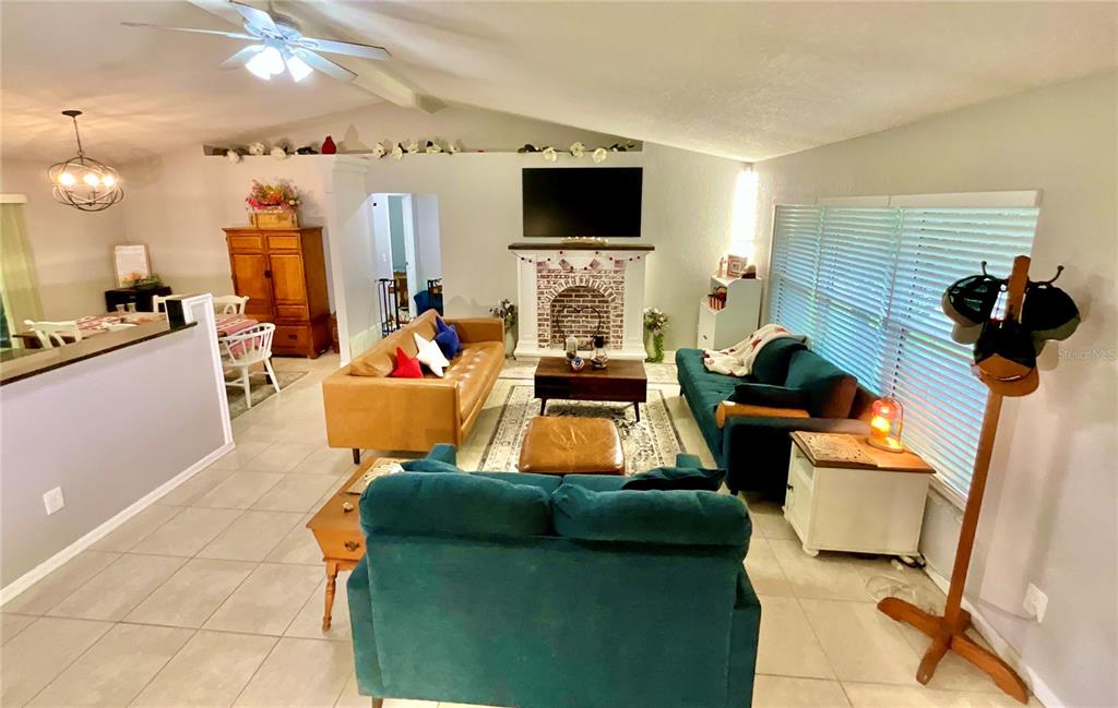 A living room features a brick fireplace, vaulted ceilings, and multiple seating areas with tile flooring — 20517 NE 114TH AVENUE, WALDO, FL