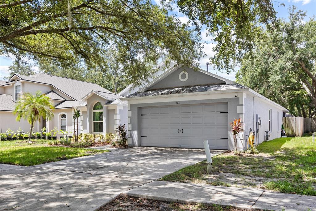 A gray house with a two-car garage and a concrete driveway under large trees — 614 SOMERSTONE DRIVE, VALRICO, FL