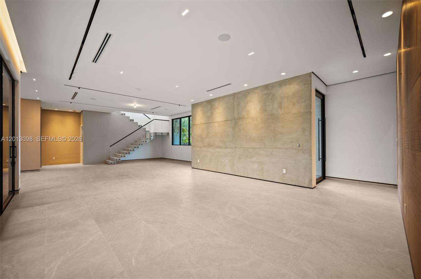 A spacious, minimalist room features large floor tiles, a concrete accent wall, and floating stairs — 7740 SW 52nd Ave, Miami FL 33143, MIAMI, FL