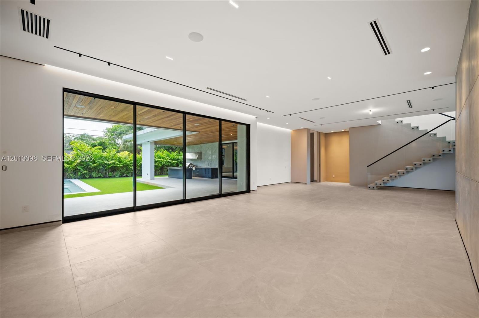 A minimalist living room features large glass sliding doors, tile flooring, and a floating staircase — 7740 SW 52nd Ave, Miami FL 33143, MIAMI, FL