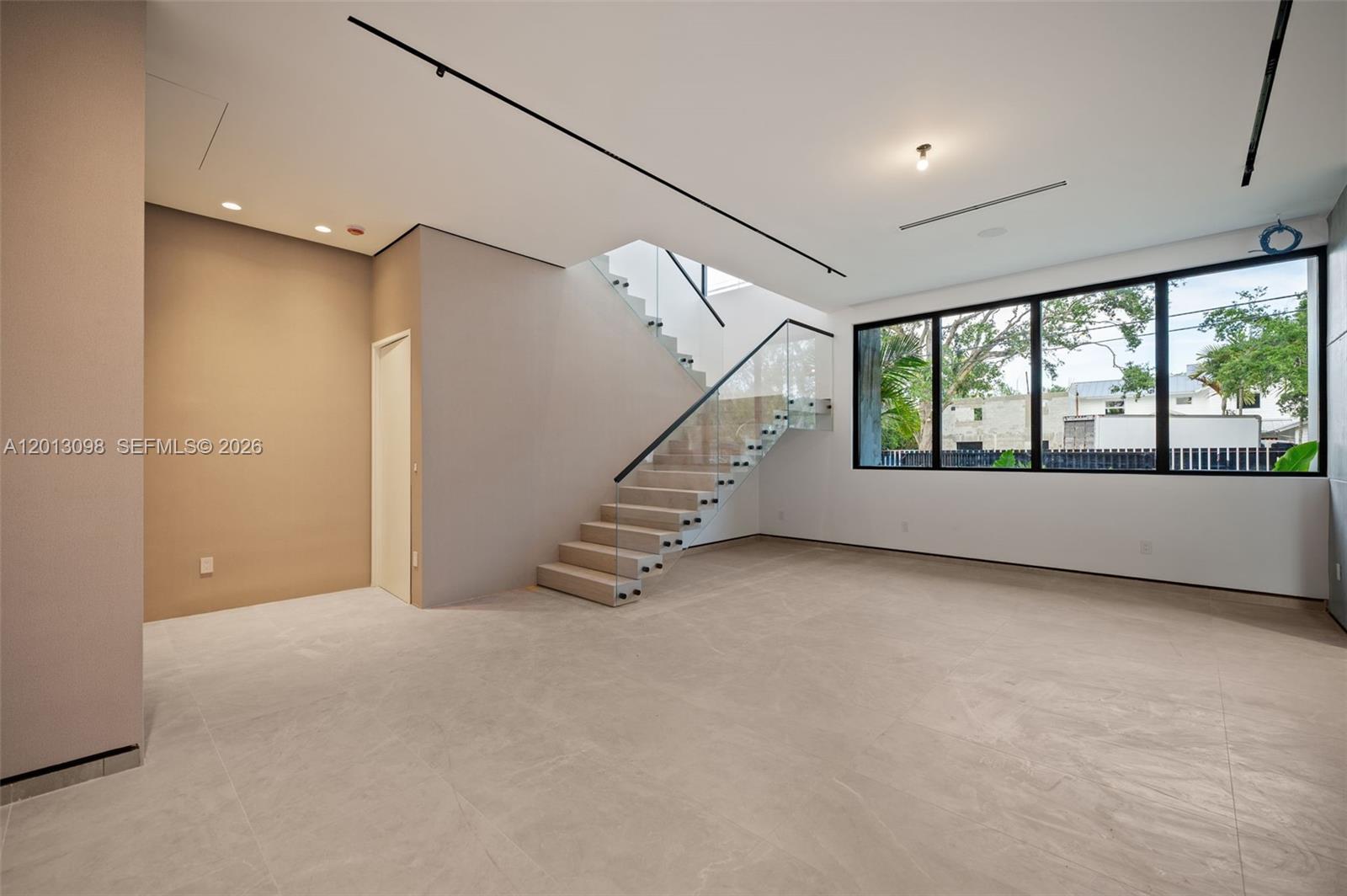 A modern room features large windows, a glass-railed staircase, and light-colored tile flooring — 7740 SW 52nd Ave, Miami FL 33143, MIAMI, FL