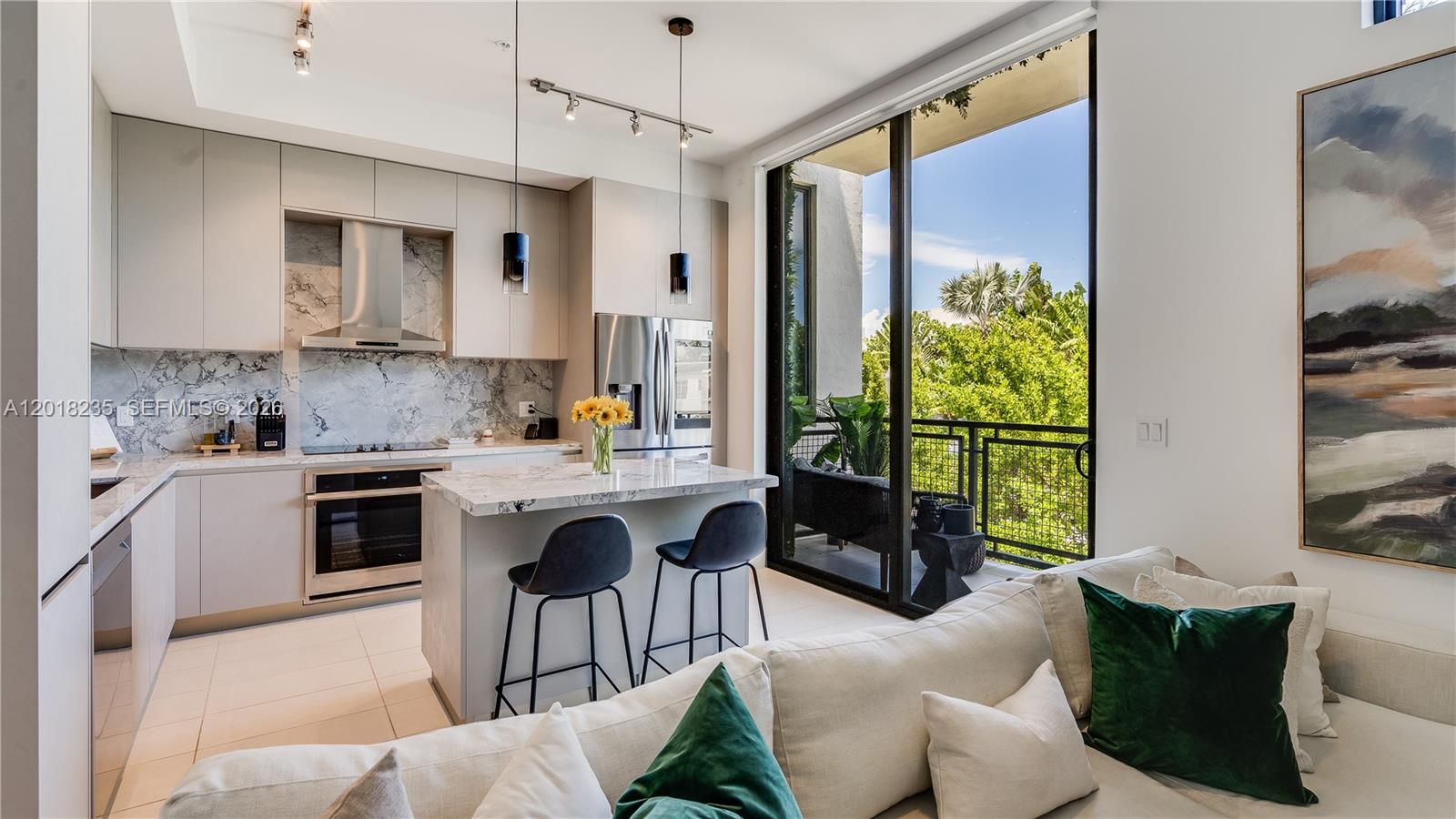 A modern kitchen with marble countertops and a breakfast bar opens to a balcony view — 1030 15th St # 201, Miami Beach FL 33139, MIAMI BEACH, FL
