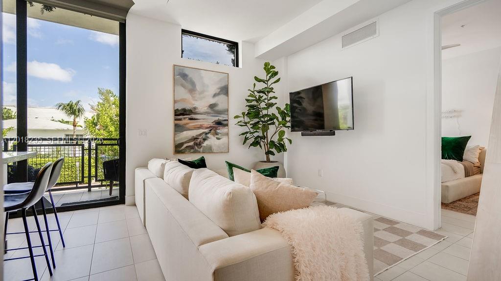 A modern living room features a white sofa, wall-mounted television, potted plant, and balcony access — 1030 15th St # 201, Miami Beach FL 33139, MIAMI BEACH, FL