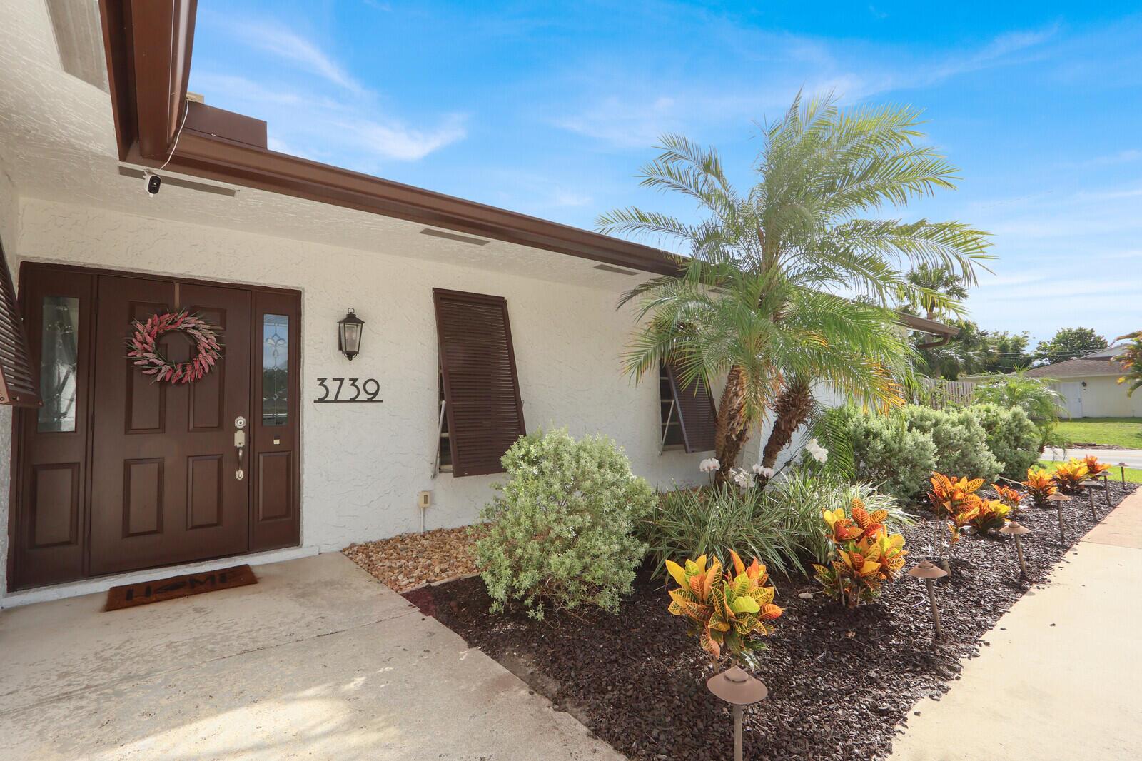 The exterior of a white house features a brown front door, shutters, and landscaping — 3739 Lighthouse Drive, Palm Beach Gardens FL 33410, PALM BEACH GARDENS, FL