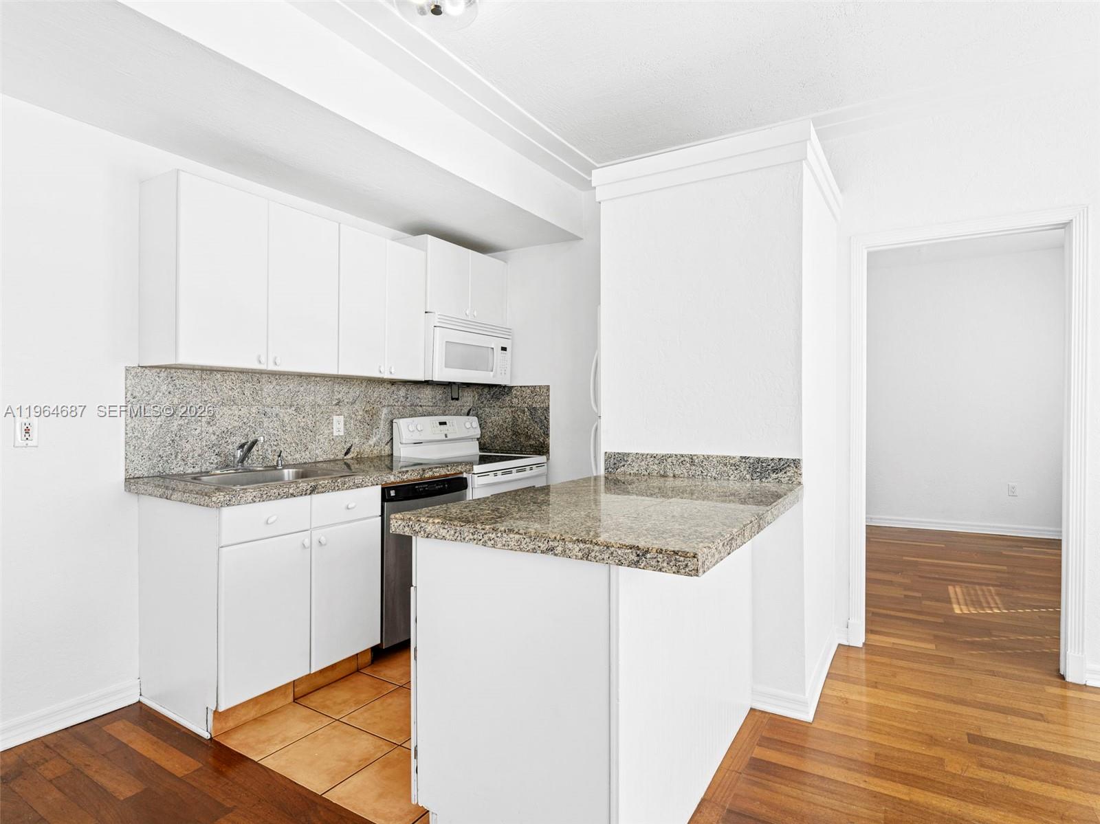 A kitchen features white cabinets, granite countertops, and a tile floor adjacent to wood flooring — 1027 Pennsylvania Ave # 206, Miami Beach FL 33139, MIAMI BEACH, FL
