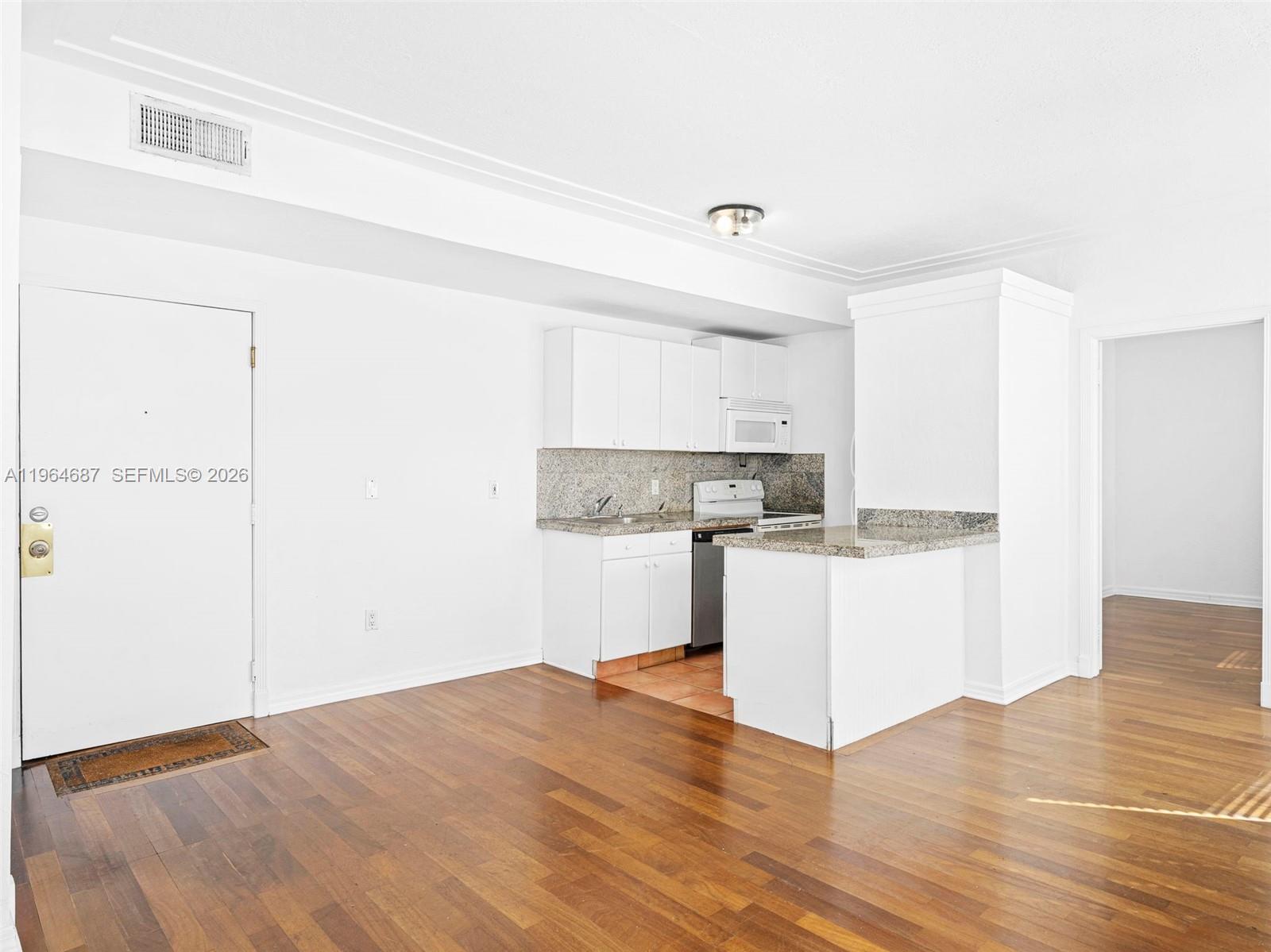 A kitchen with white cabinets and granite countertops opens into a wood-floored living area — 1027 Pennsylvania Ave # 206, Miami Beach FL 33139, MIAMI BEACH, FL