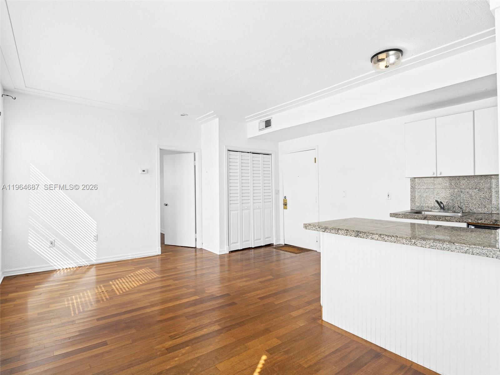 An open-concept living area features hardwood flooring, a kitchen counter, and white cabinetry — 1027 Pennsylvania Ave # 206, Miami Beach FL 33139, MIAMI BEACH, FL