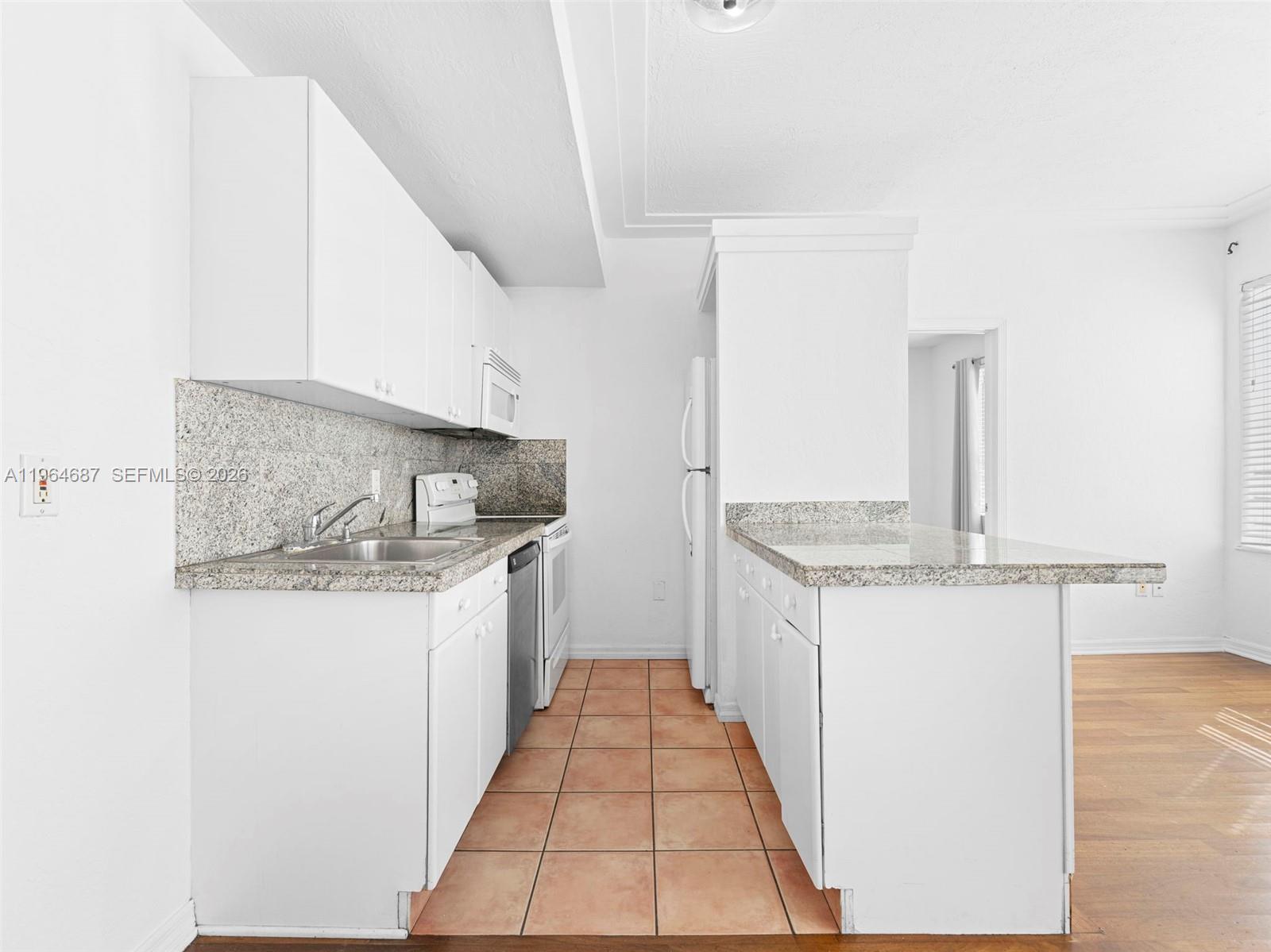 A kitchen features white cabinets, granite countertops, a stainless steel dishwasher, and tiled flooring — 1027 Pennsylvania Ave # 206, Miami Beach FL 33139, MIAMI BEACH, FL