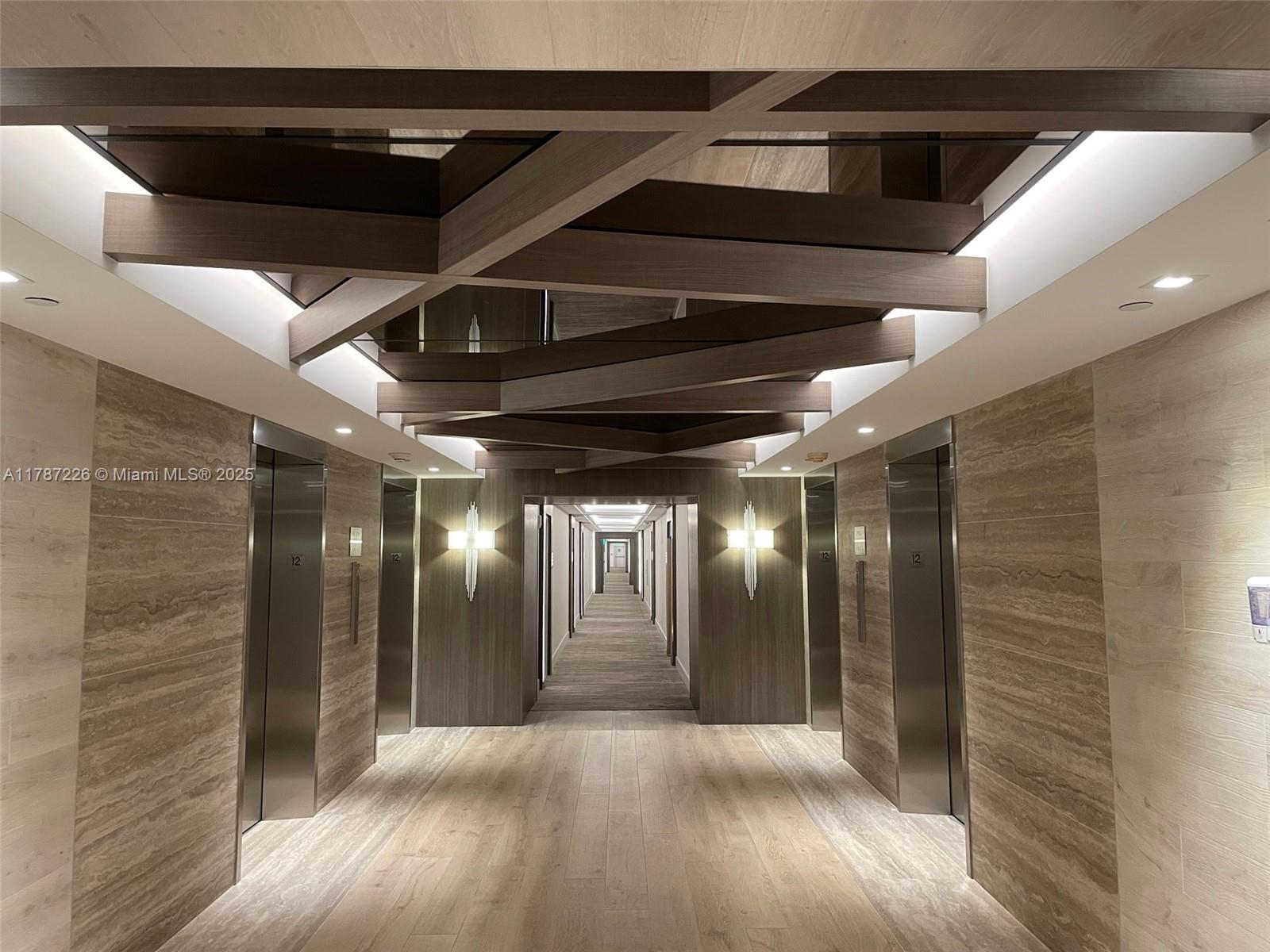 A modern elevator lobby features wood-paneled walls, a geometric ceiling design, and a long hallway — 2301 COLLINS AV, Miami Beach FL 33139, MIAMI BEACH, FL