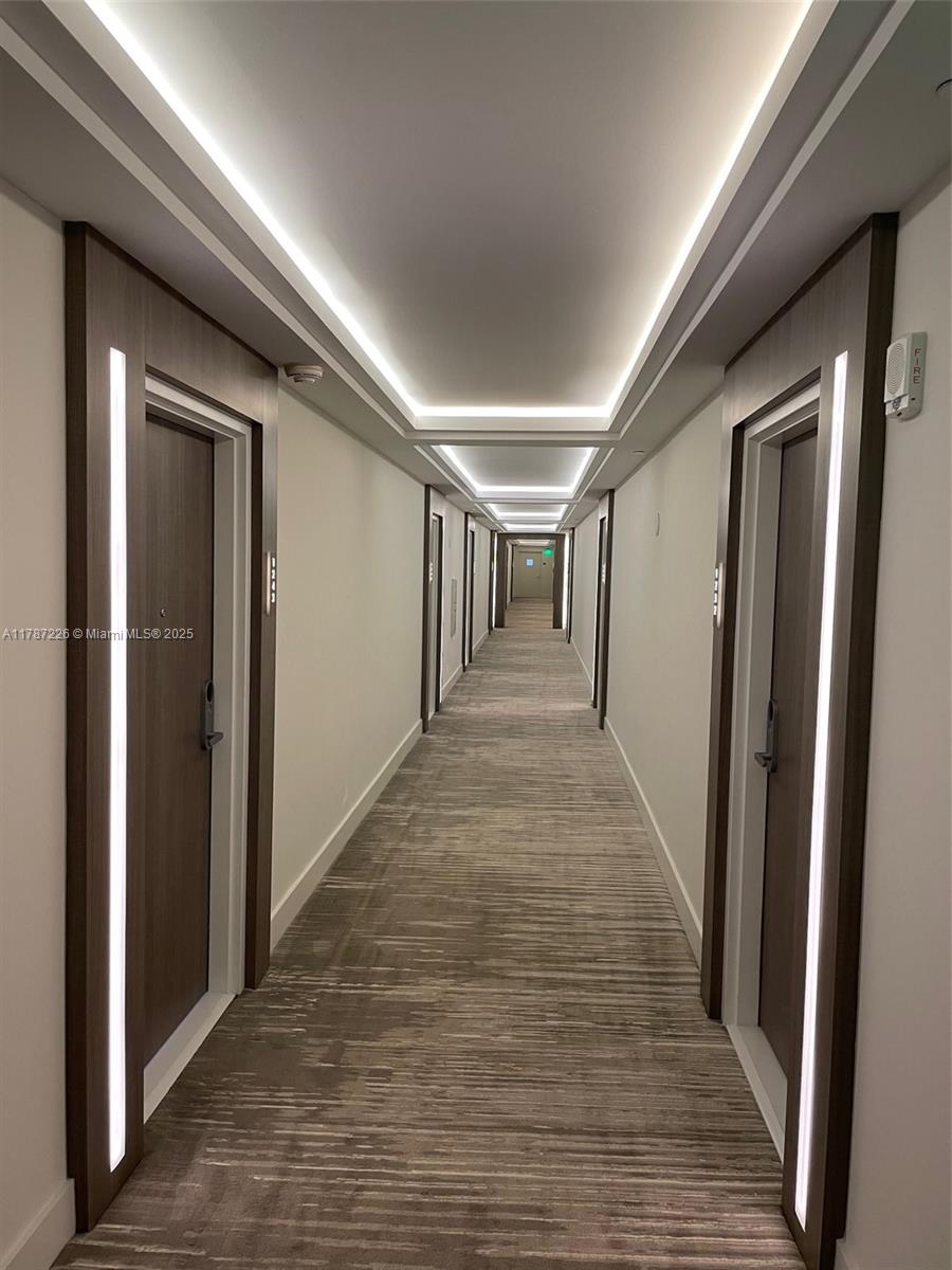 A long, narrow hotel-style hallway features recessed ceiling lighting and doors with vertical light panels — 2301 COLLINS AV, Miami Beach FL 33139, MIAMI BEACH, FL
