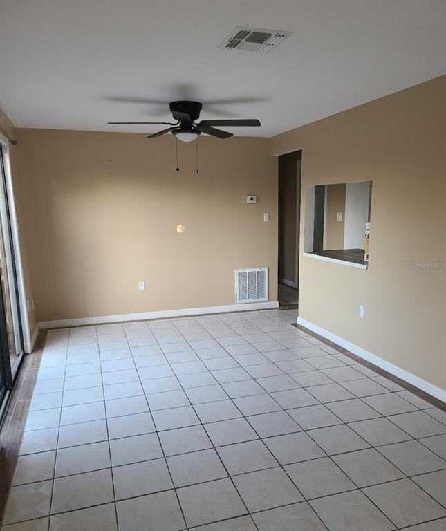 A dining room with beige walls, white tile flooring, a ceiling fan, and a pass-through window — 4925 SANOMA VLG UNIT C, ORLANDO, FL