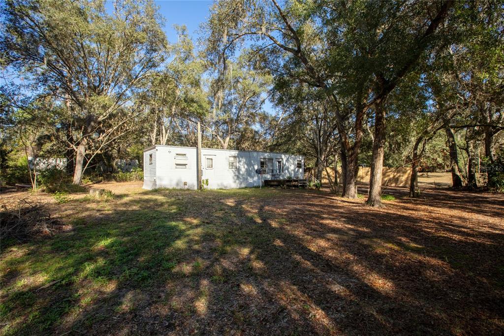 A single-story mobile home sits in a wooded yard with scattered leaves and tall trees — 270 BAY STREET, HAWTHORNE, FL