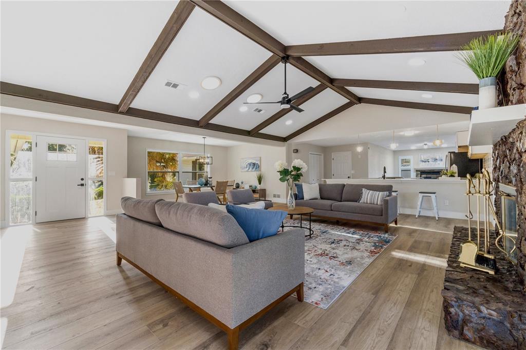 A living room features vaulted ceilings with exposed beams, a stone fireplace, and wood flooring — 5391 NW 76TH COURT, OCALA, FL