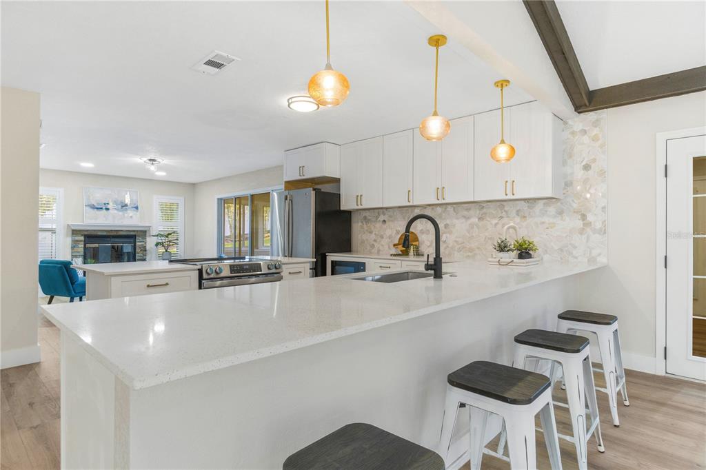 A modern kitchen features white cabinets, quartz countertops, a tile backsplash, and three bar stools — 5391 NW 76TH COURT, OCALA, FL