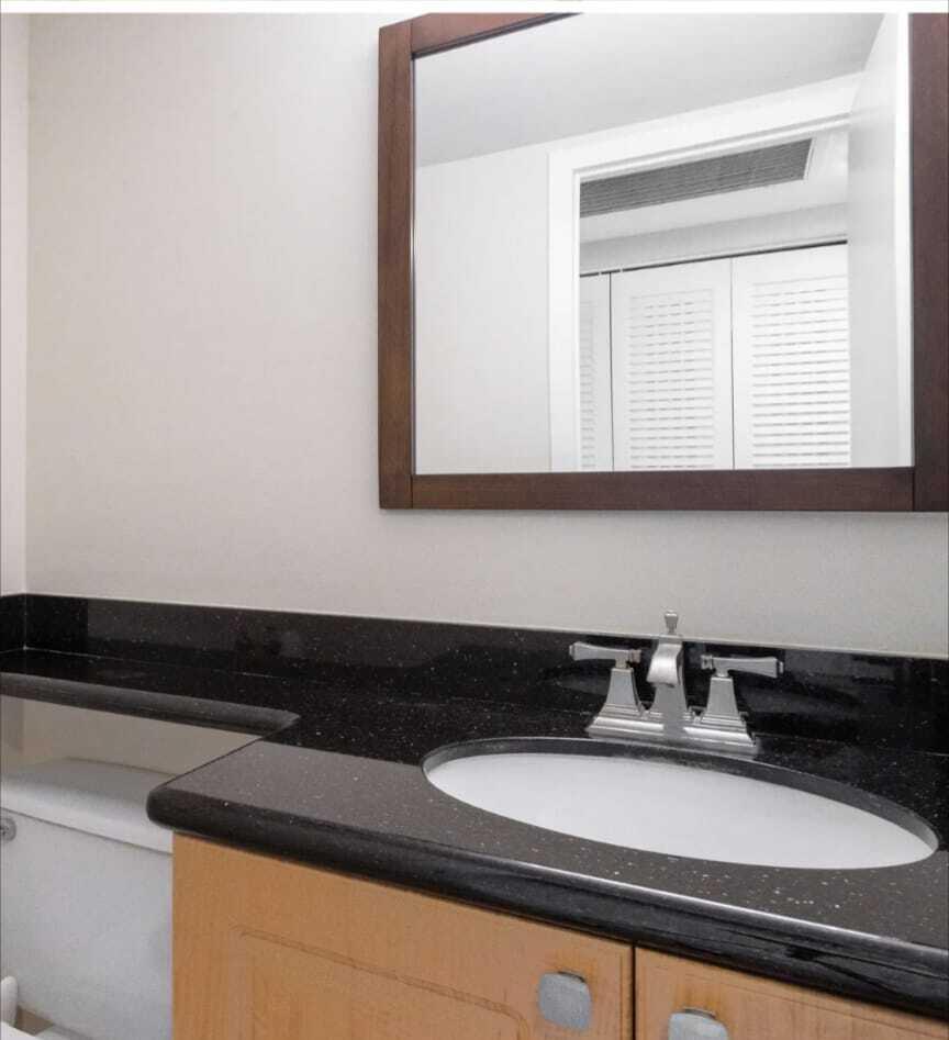 A bathroom vanity features a black granite countertop, a white sink, and a wooden cabinet — 2053 Cornwall C, Boca Raton FL 33434, BOCA RATON, FL