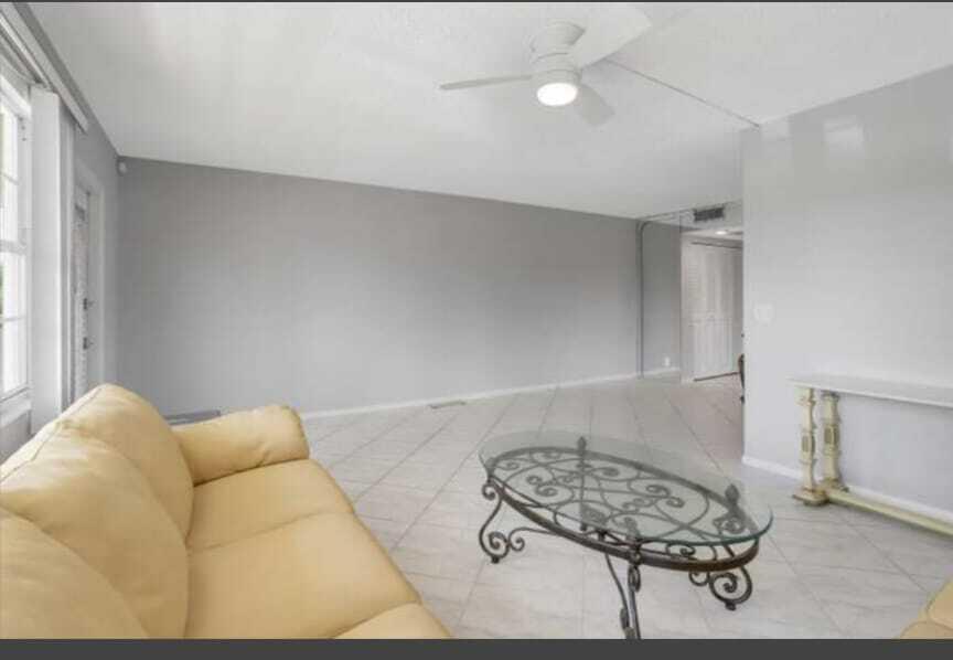 A living room features a yellow sofa, a glass coffee table, and light-colored tile flooring — 2053 Cornwall C, Boca Raton FL 33434, BOCA RATON, FL