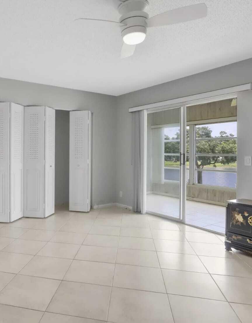 A room with light tile flooring, a ceiling fan, white folding closet doors, and sliding doors — 2053 Cornwall C, Boca Raton FL 33434, BOCA RATON, FL