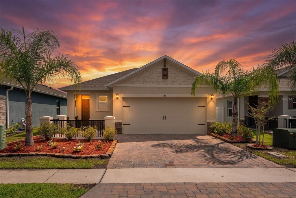 A single-story house with a two-car garage, paved driveway, and palm trees at sunset — 281 CARYOTA COURT, NEW SMYRNA BEACH, FL