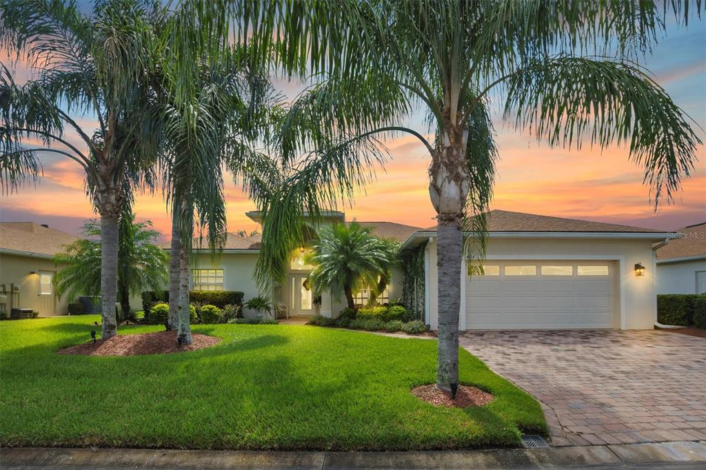 A single-story house with a paved driveway, palm trees, and a sunset sky in the background — 4315 ASHTON CLUB DRIVE, LAKE WALES, FL