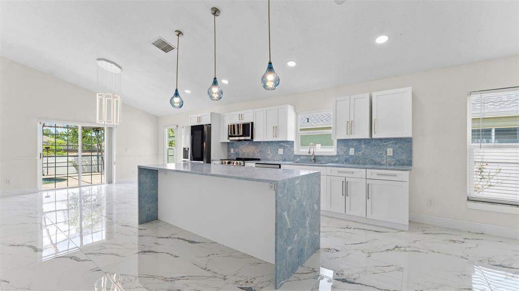 A modern kitchen features white cabinets, blue marble countertops, and a matching waterfall island — 11708 CARROLLWOOD COVE DRIVE, TAMPA, FL