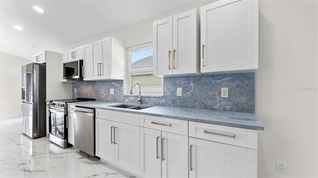 A kitchen features white cabinets, blue marble-patterned countertops, a backsplash, and stainless steel appliances — 11708 CARROLLWOOD COVE DRIVE, TAMPA, FL