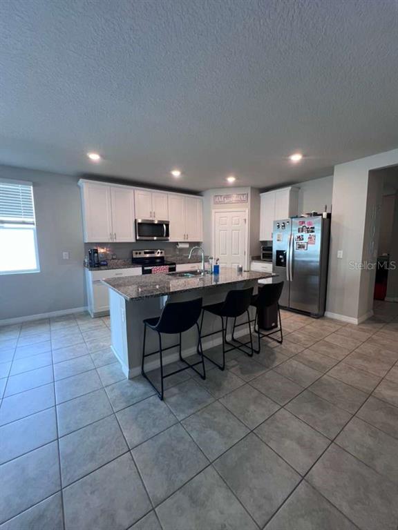 A kitchen features white cabinets, a granite-topped island with bar stools, and stainless steel appliances — 560 JERRY LN, HAINES CITY, FL