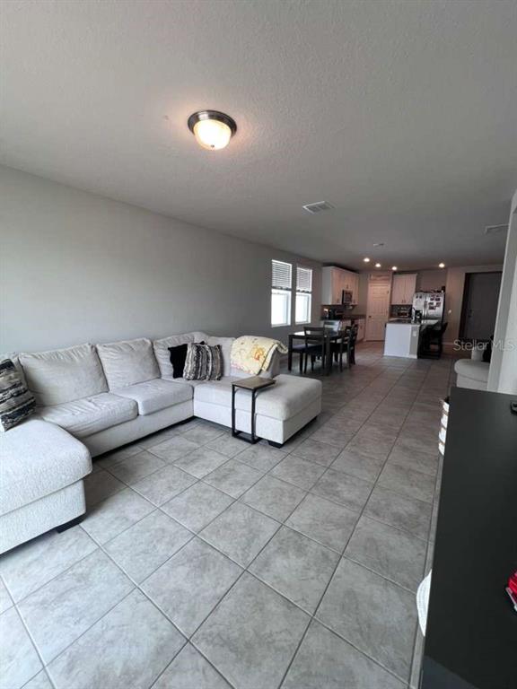 An open-concept living room features a large sectional sofa, tile flooring, and an adjacent kitchen — 560 JERRY LN, HAINES CITY, FL