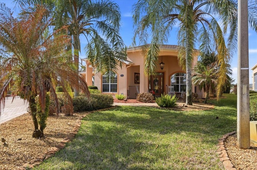 A single-story stucco house with a covered entryway, palm trees, and a landscaped front yard — 548 MEANDERING WAY, POLK CITY, FL
