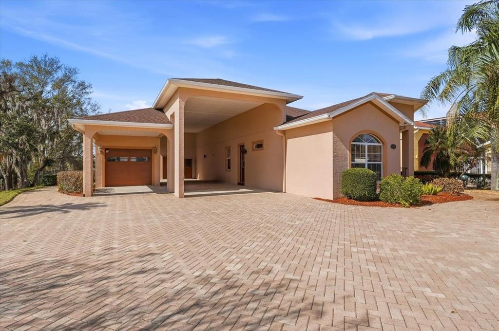 A peach-colored house with a large covered carport and a brick paver driveway — 548 MEANDERING WAY, POLK CITY, FL