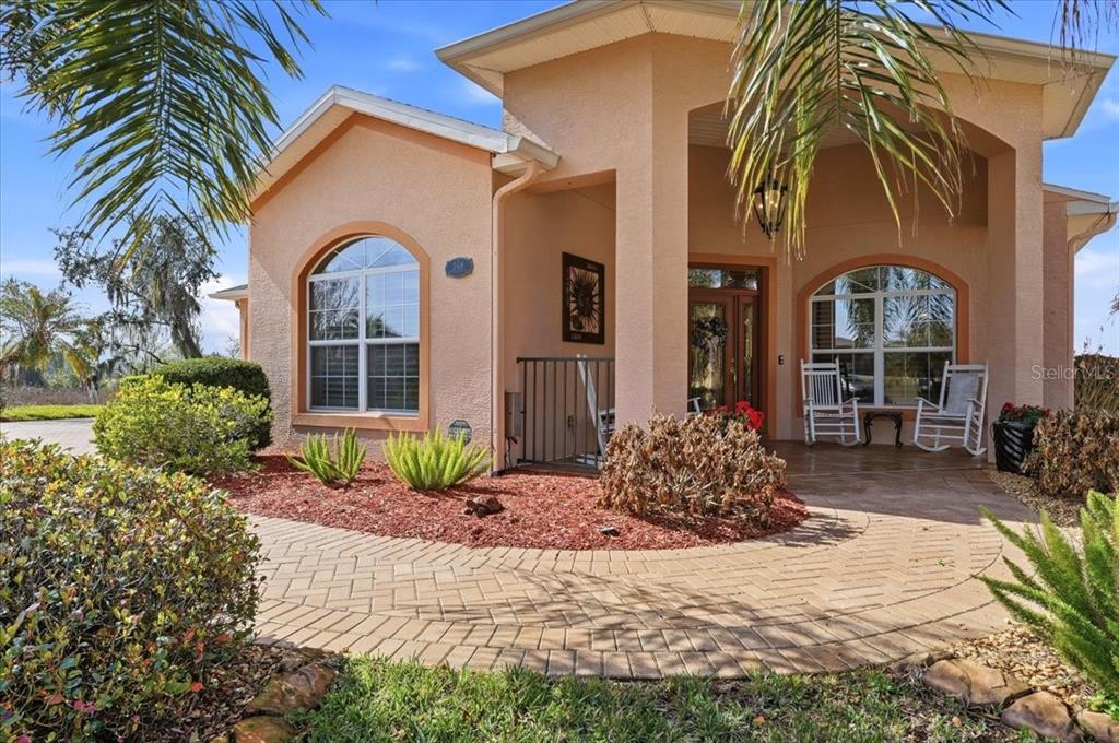 A single-story house with a tan stucco exterior, arched windows, and a paved front walkway — 548 MEANDERING WAY, POLK CITY, FL