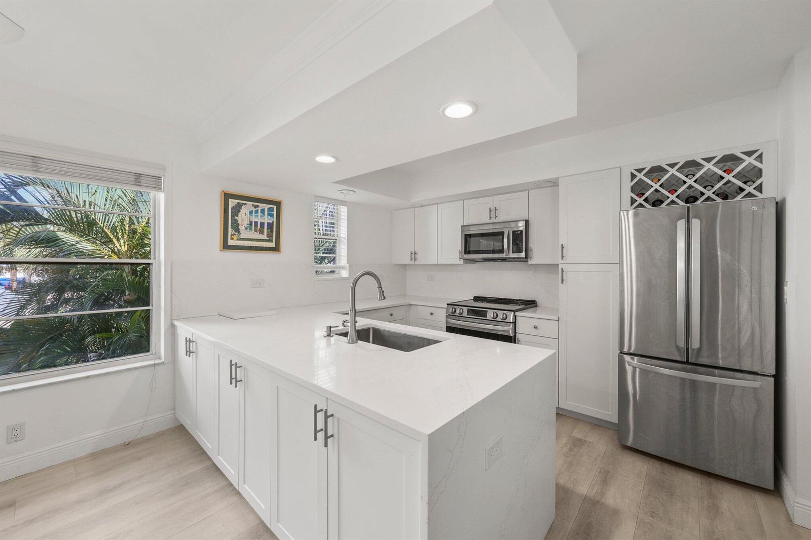 A modern white kitchen features a large island, stainless steel appliances, and a wine rack — 664 Forsyth Street # 6, Boca Raton FL 33487, BOCA RATON, FL