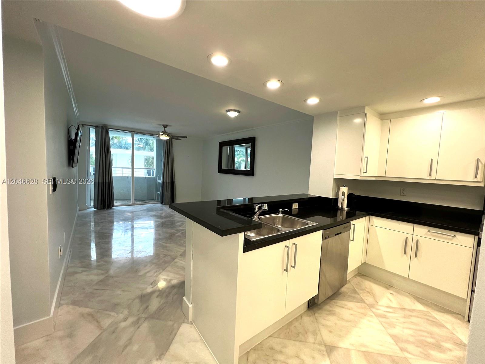 A kitchen with black countertops and white cabinets opens into a living area with balcony — 200 Ocean Dr # 3C, Miami Beach FL 33139, MIAMI BEACH, FL