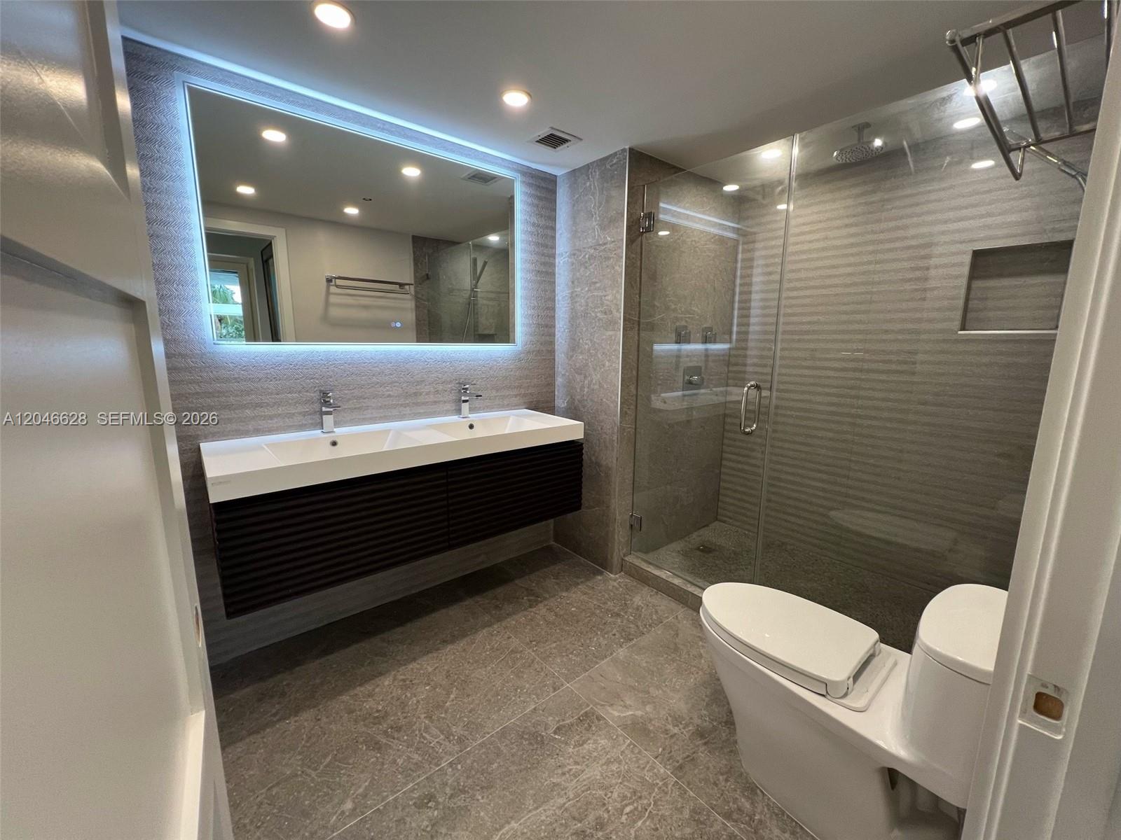 A modern bathroom features a double vanity, a glass-enclosed shower, and gray tile flooring — 200 Ocean Dr # 3C, Miami Beach FL 33139, MIAMI BEACH, FL