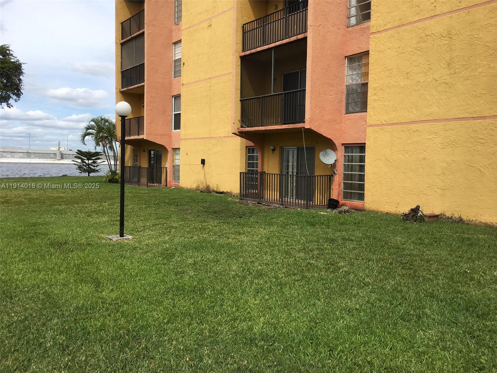 The exterior of a yellow and peach apartment building features balconies and a grassy lawn — 4719 NW 7th St # 11, Miami FL 33126, MIAMI, FL
