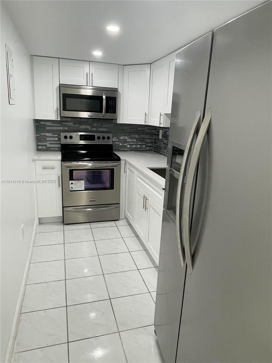 A galley kitchen features white cabinets, stainless steel appliances, and a gray tiled backsplash — 4719 NW 7th St # 11, Miami FL 33126, MIAMI, FL