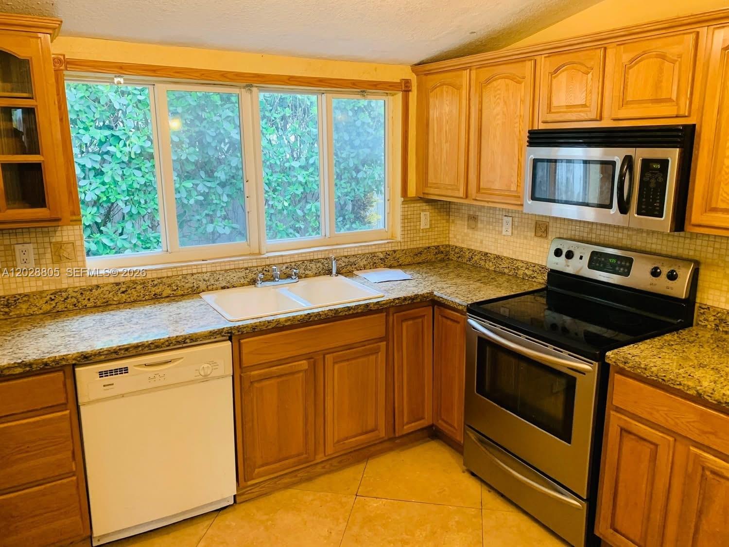 A kitchen features wood cabinets, granite countertops, a white dishwasher, and stainless steel appliances — 6134 SW 22nd St, Miami FL 33155, MIAMI, FL