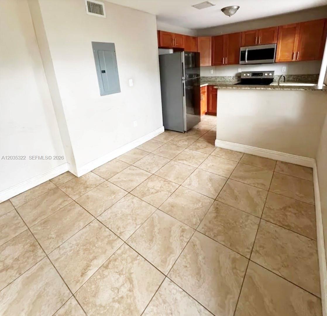 A kitchen with wood cabinets and stainless steel appliances opens to a tiled dining area — 1999 NW 5th Pl # 2, Miami FL 33136, MIAMI, FL