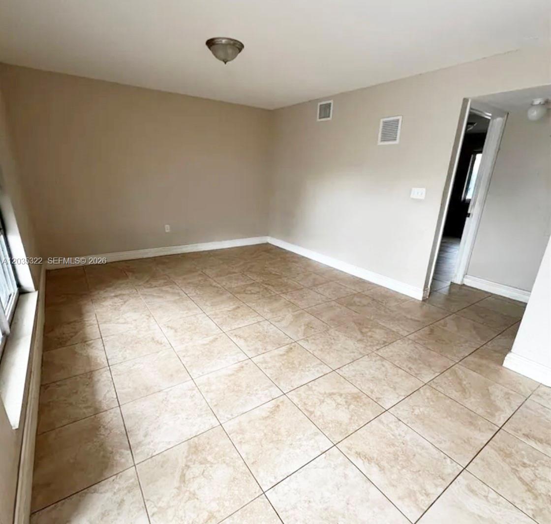An empty room features beige walls, light-colored tile flooring, and a single ceiling light fixture — 1999 NW 5th Pl # 2, Miami FL 33136, MIAMI, FL
