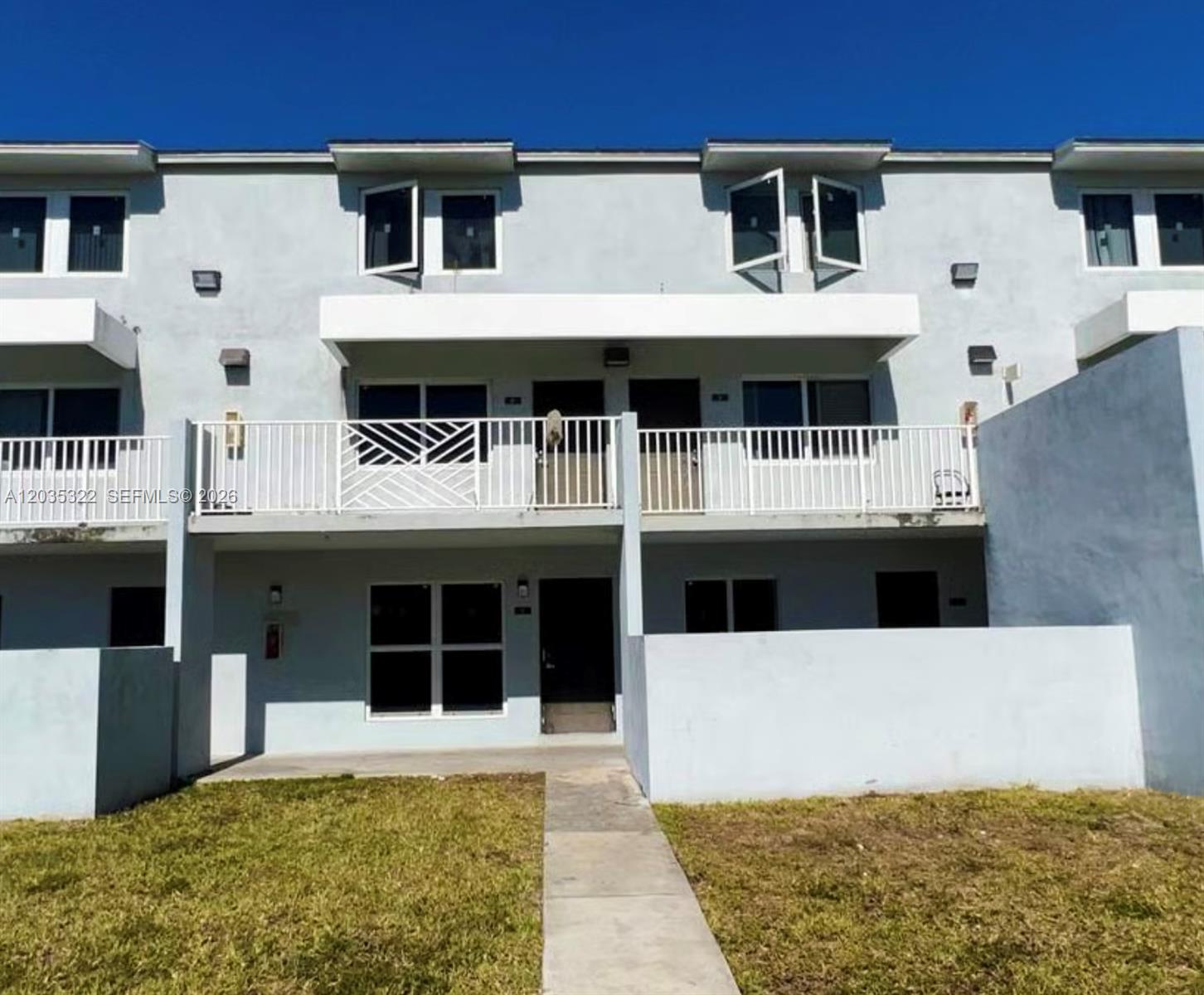 A two-story townhouse exterior features a white balcony, concrete walls, and a small lawn — 1999 NW 5th Pl # 2, Miami FL 33136, MIAMI, FL