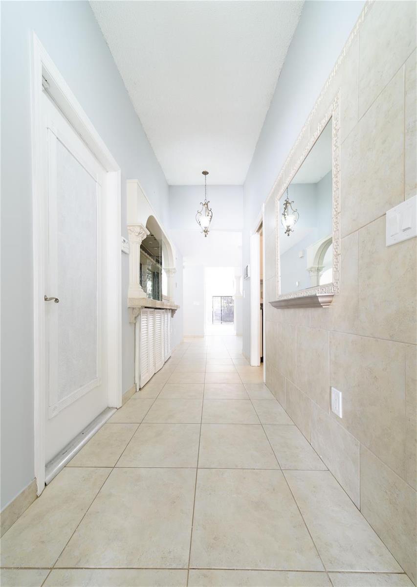 A hallway with light-colored tile flooring, a mirror on a tiled wall, and a pendant light — 6680 Canary Palm Circle, Boca Raton FL 33433, BOCA RATON, FL