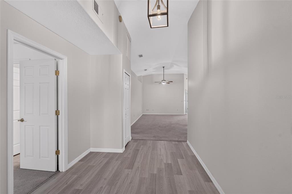 A hallway with wood-look flooring leads to a carpeted living area with a vaulted ceiling — 1514 ORACLE DRIVE, SUN CITY CENTER, FL