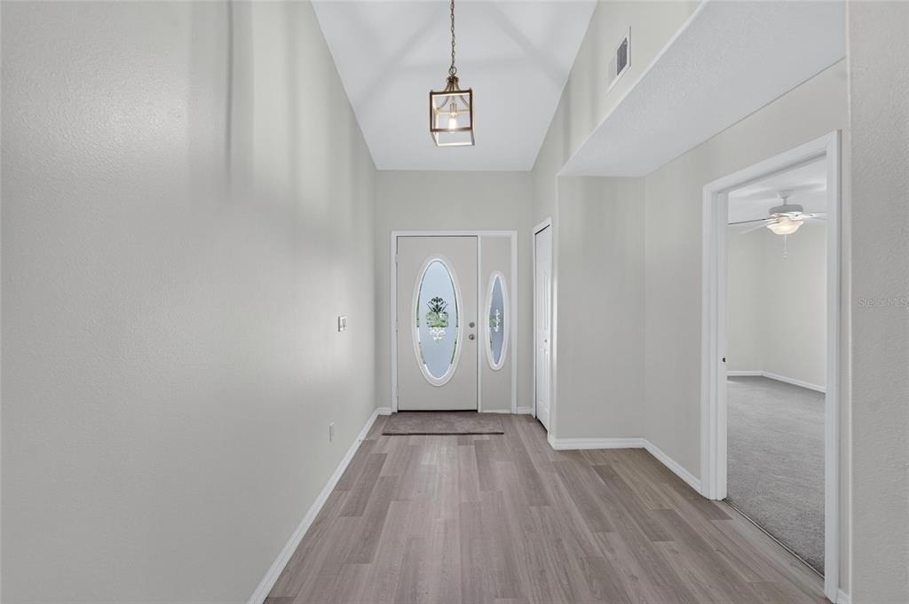 A bright entryway features light wood-look flooring, a vaulted ceiling, and a decorative front door — 1514 ORACLE DRIVE, SUN CITY CENTER, FL