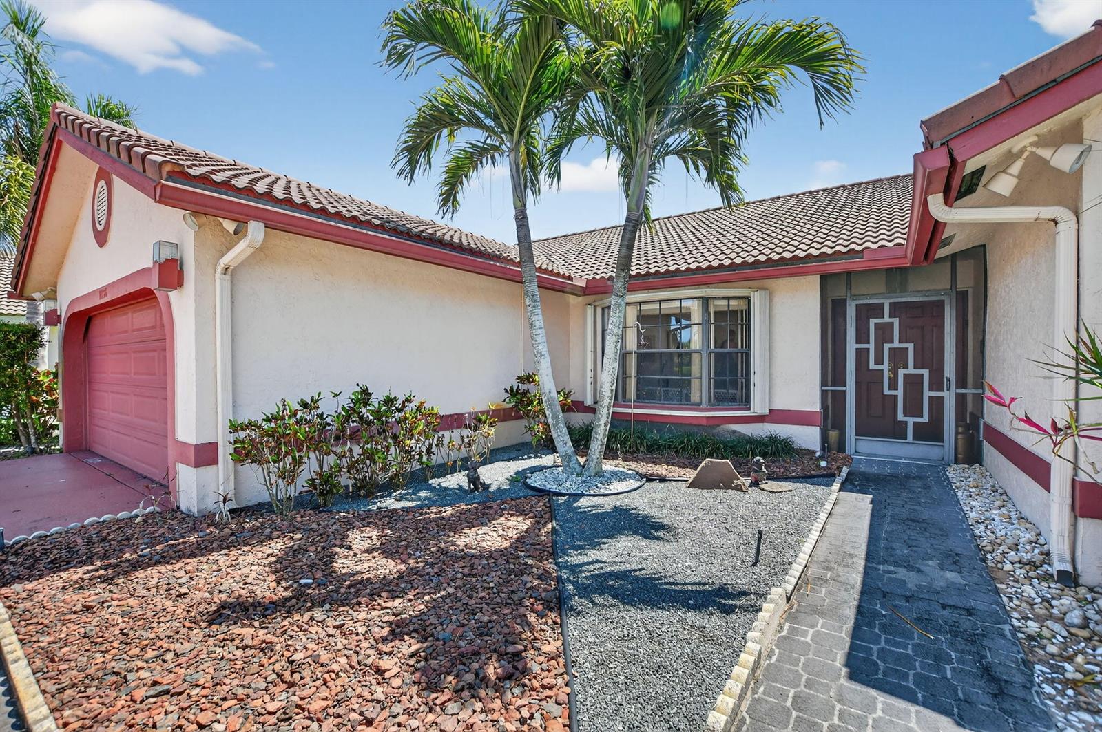 The exterior of a house features a red garage door, palm trees, and gravel landscaping — 10226 Fresh Meadow Lane, Boca Raton FL 33498, BOCA RATON, FL