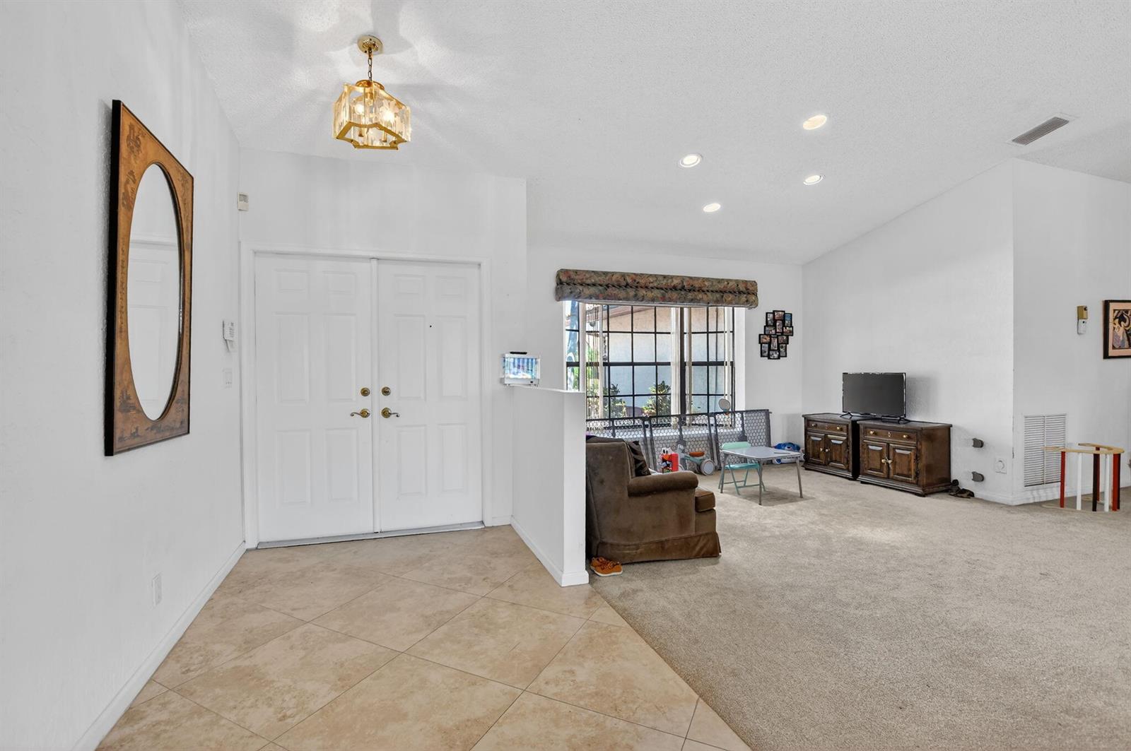 A foyer with tile flooring leads into a carpeted living area with a double door entrance — 10226 Fresh Meadow Lane, Boca Raton FL 33498, BOCA RATON, FL